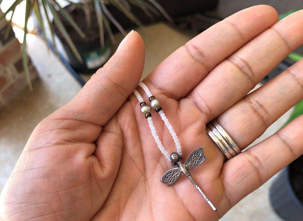 black woman's hand holding a dragonfly necklace