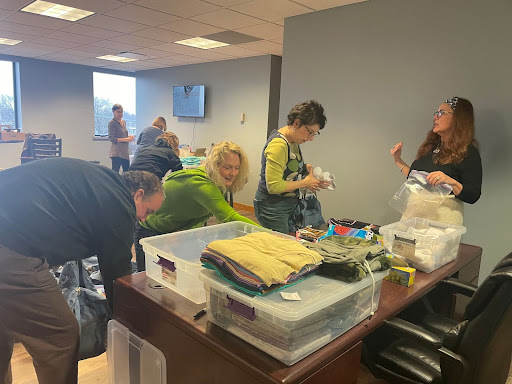 volunteers assembling SOS kits. there are clothes and plastic boxes on a table.